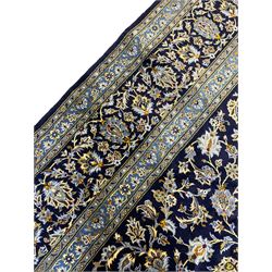 Central Persian Kashan indigo ground carpet, central lighter blue floral medallion surrounded by interlacing leafy branches and stylised plant motifs, the main border decorated with repeating floral motifs and scrolling branches, within guard stripes 