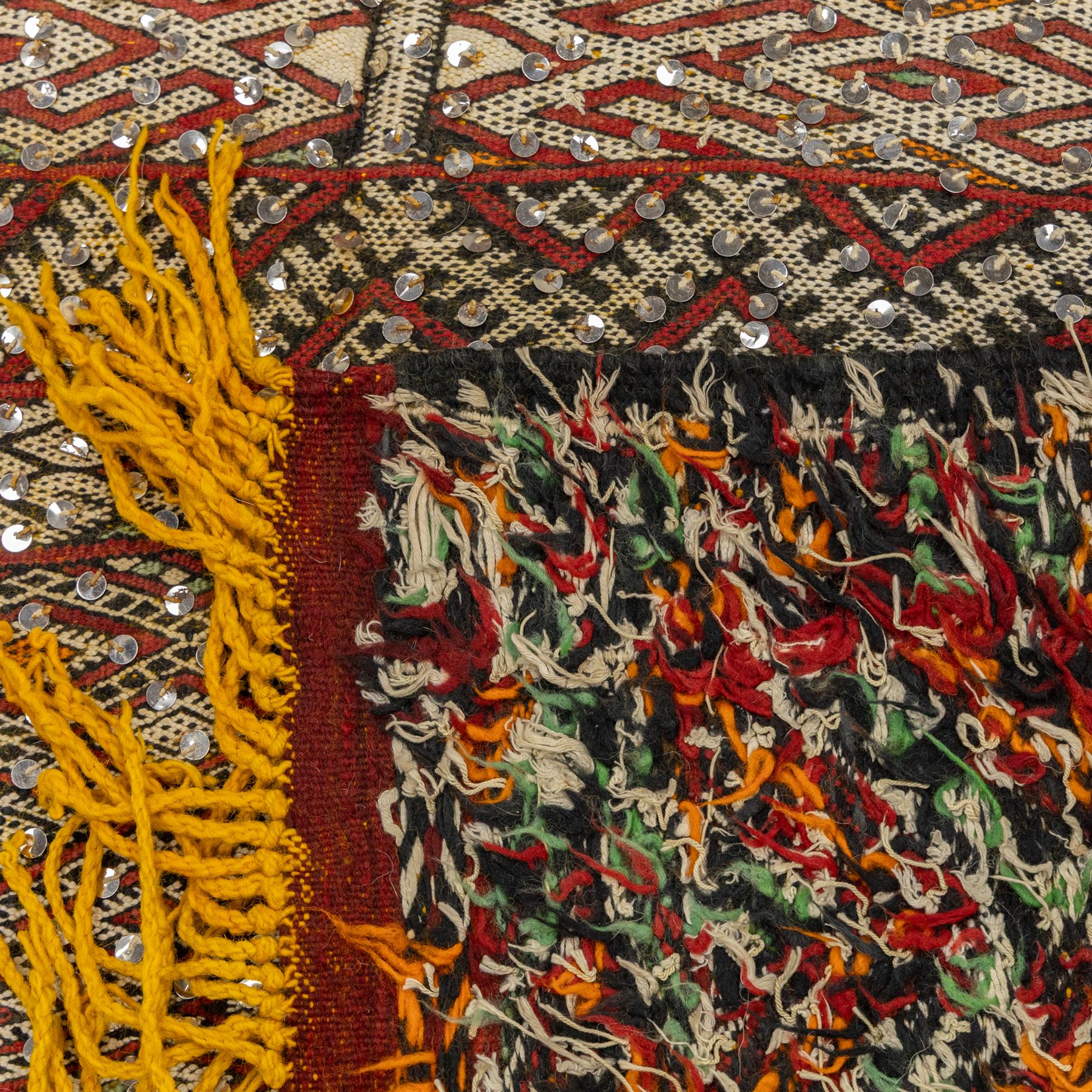 Moroccan Berber kilim rug, flatwoven with bands of geometric lozenge and chevron motifs in red, orange, ivory and green, decorated with applied sequins, fringed ends