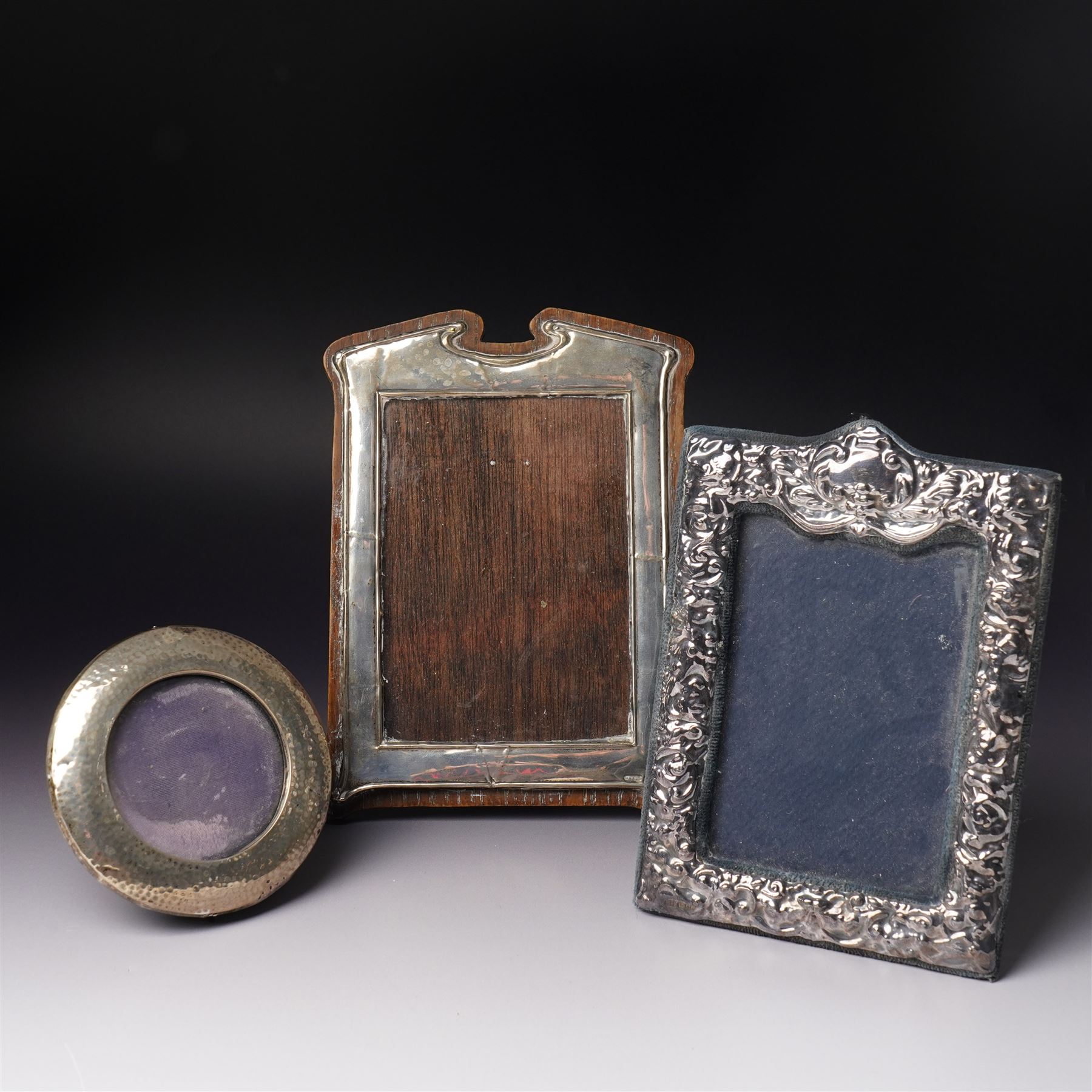 Embossed silver photograph frame London 1985 aperture 12.5cm x 8.5cm, another with scroll top Birmingham 1921 13cm x 9cm and a circular frame Birmingham 1909 6cm