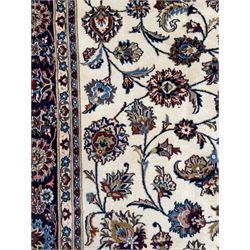 Northeastern Persian Meshed hand-knotted rug, ivory ground with an overall design of scrolling vines, palmettes, and rosettes in an indigo palette, soft blues, and madder, framed by a deep indigo border of lotus palmettes and flowerheads between multiple guard borders, 300cm x 202cm
