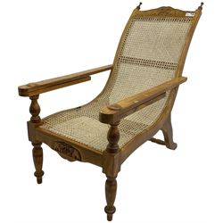 Late 20th century teak framed plantation chair, cresting rail and apron carved with two elephants with upraised trunks, flanked by finials, cane back and seat, fitted with hinged extending leg rests, on ring turned supports