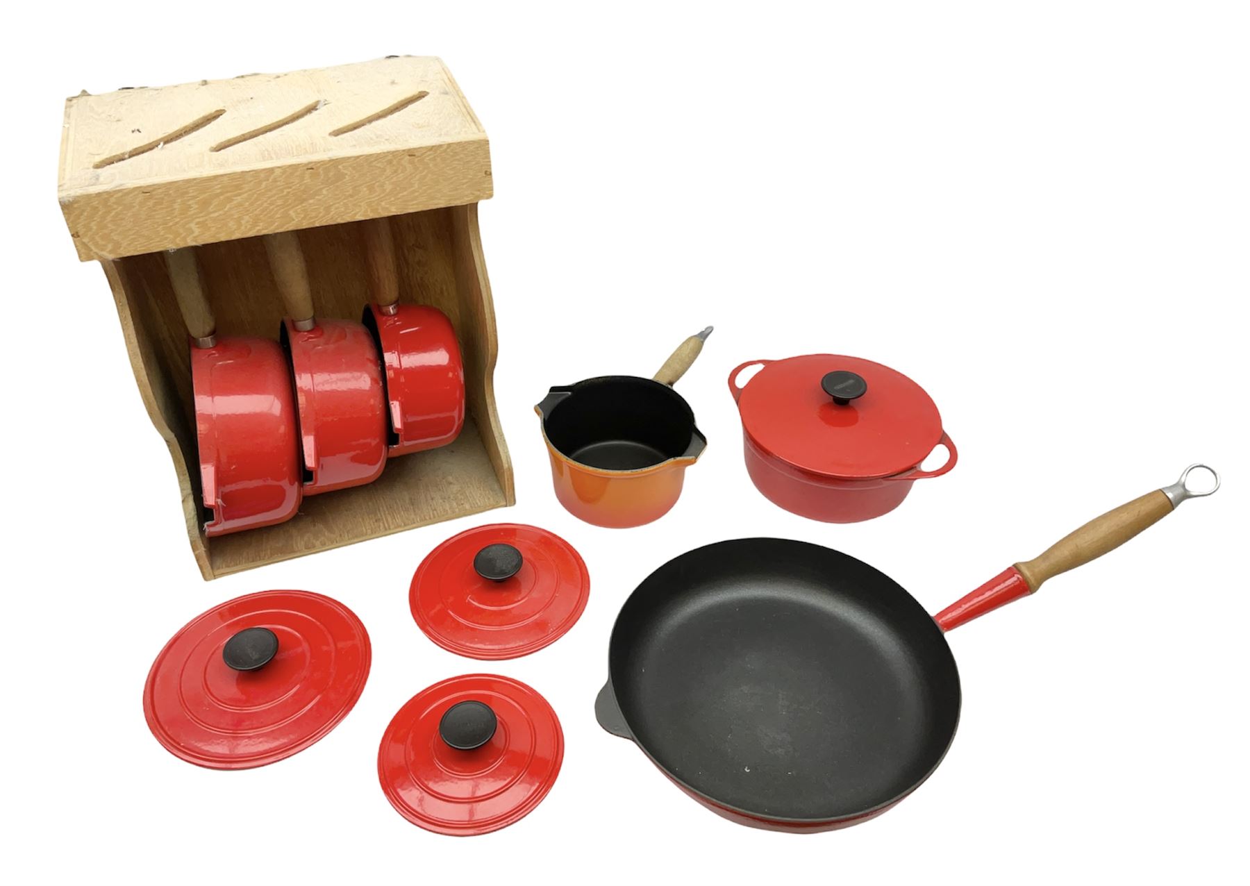 Le Creuset 'Volcanic Orange' cast iron and enamel milk pan with wood handle together with a three piece red cast iron Cousances saucepan set of graduating form, with lids housed in original wooden hanging stand and further Cousances lidded casserole dish and pan