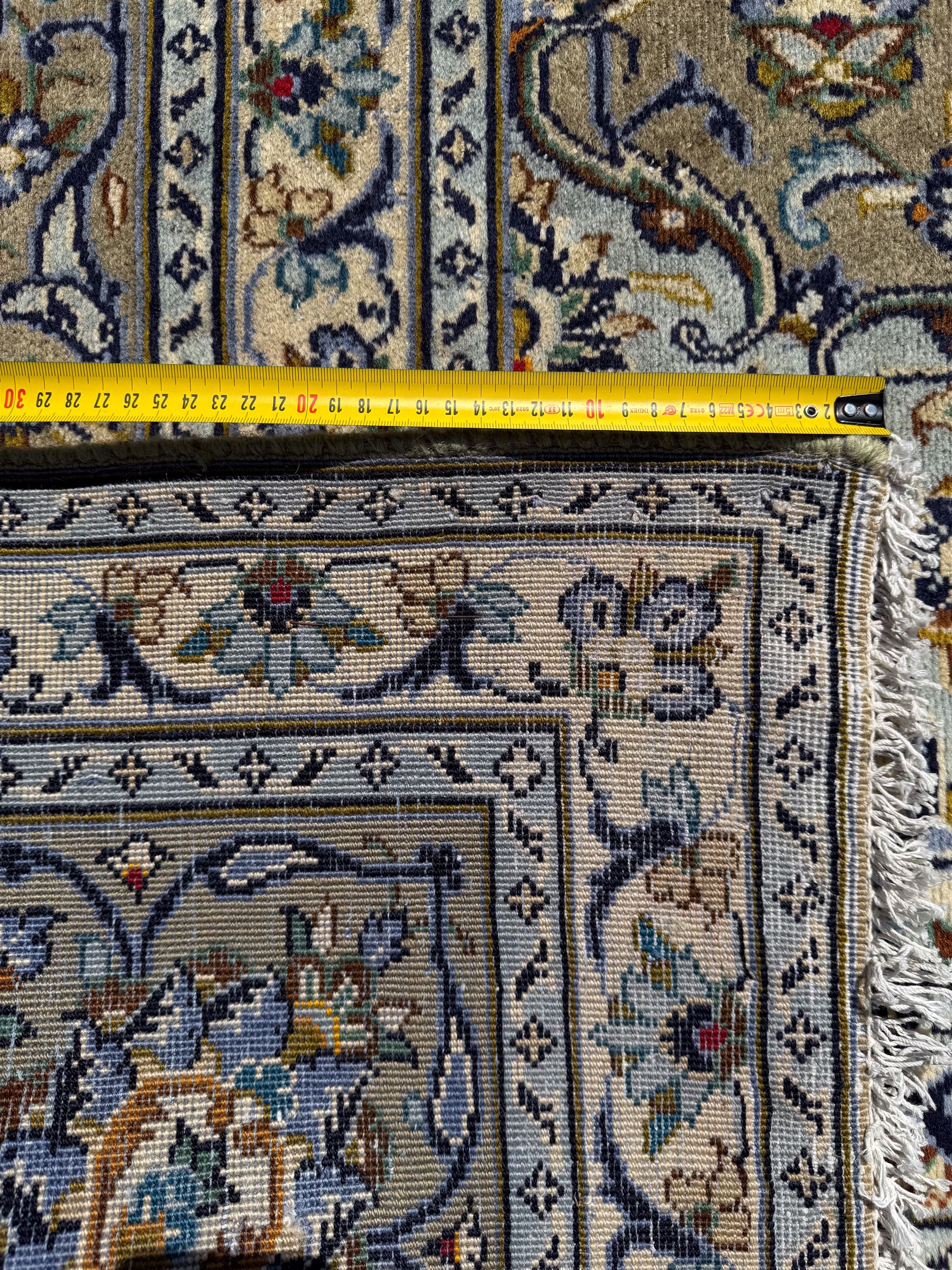 Central Persian Kashan pale khaki and ivory ground carpet, shaped central medallion enclosing small stylised motifs, the field decorated profusely with trailing foliate branches and plant motifs, guarded border with repeating floral design