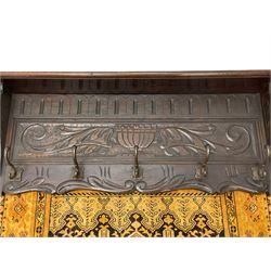 20th century oak wall hanging coat rack with hanging, projecting moulded lintel over panel carved with urn and extending scrolling foliage, decorated with carved masks, fitted with five metal hooks