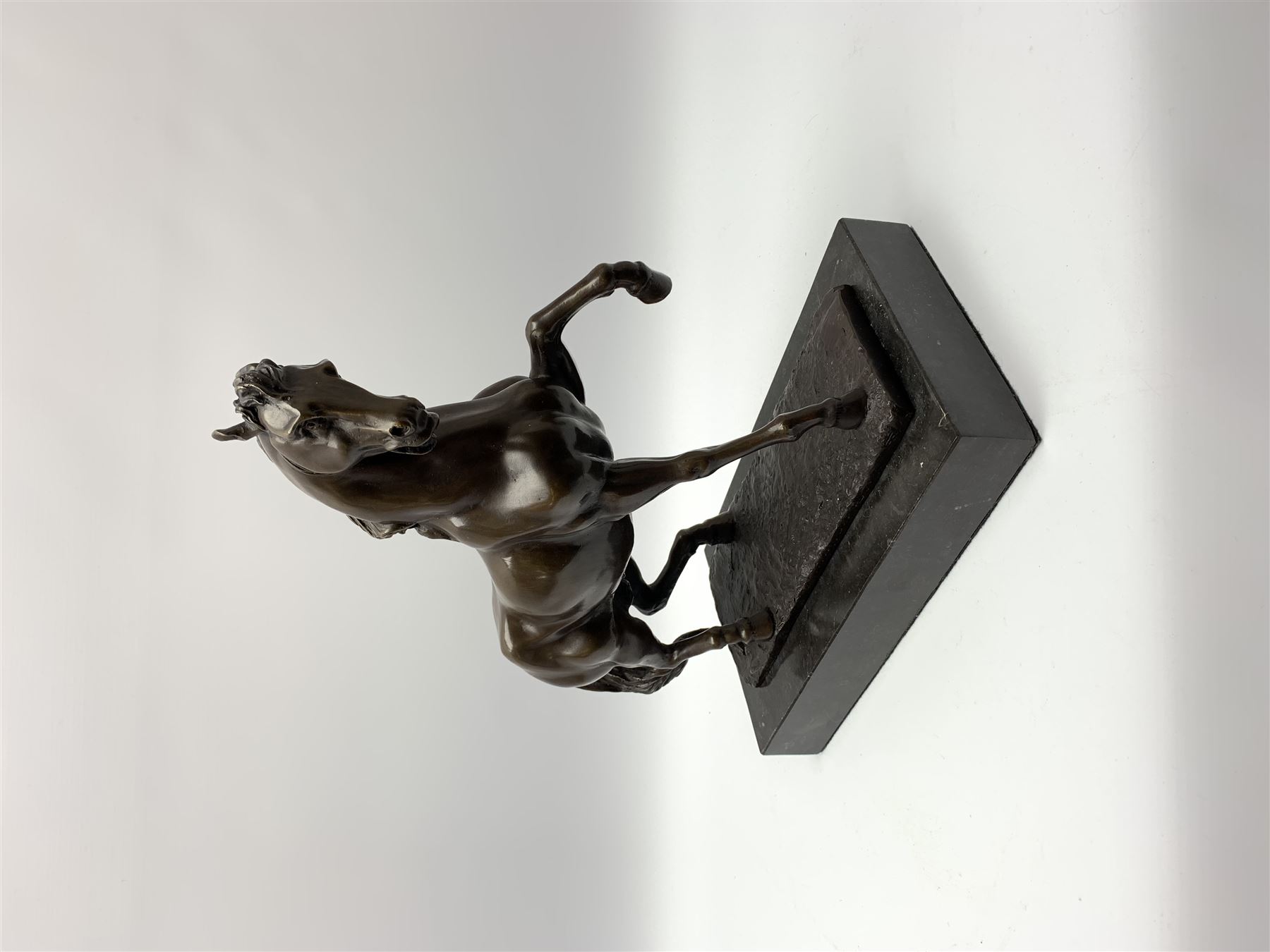 Bronze figure modelled as a prancing horse, upon a naturalistically modelled rectangular base, and black marble plinth, H34.5cm, L31cm