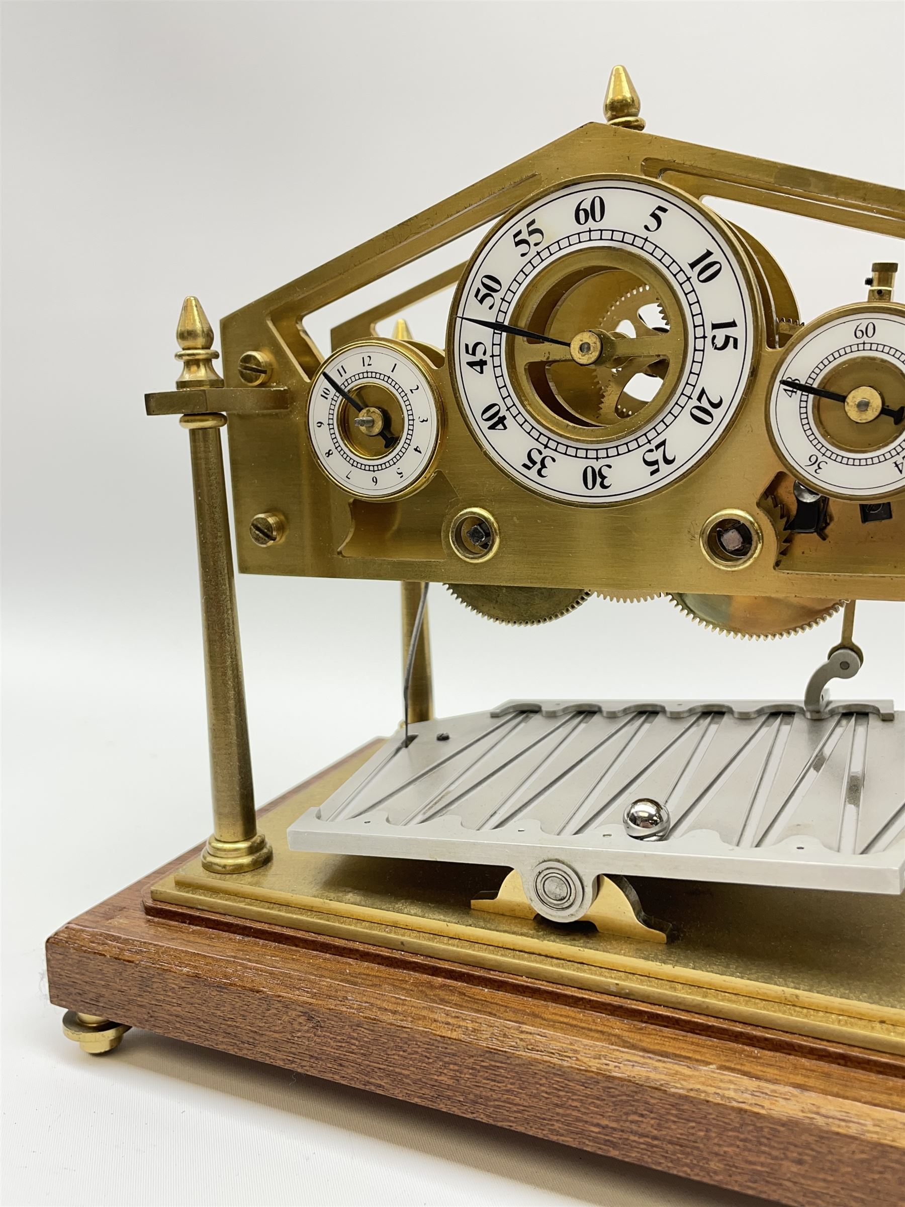 Mid 20th century 'Congreve' rolling ball clock, sloped arch and pierced brass movement, the central Arabic minute chapter ring flanked by hour and seconds dials, twin train driven eight day movement, raised on mahogany plinth with turned brass feet, under acrylic cover