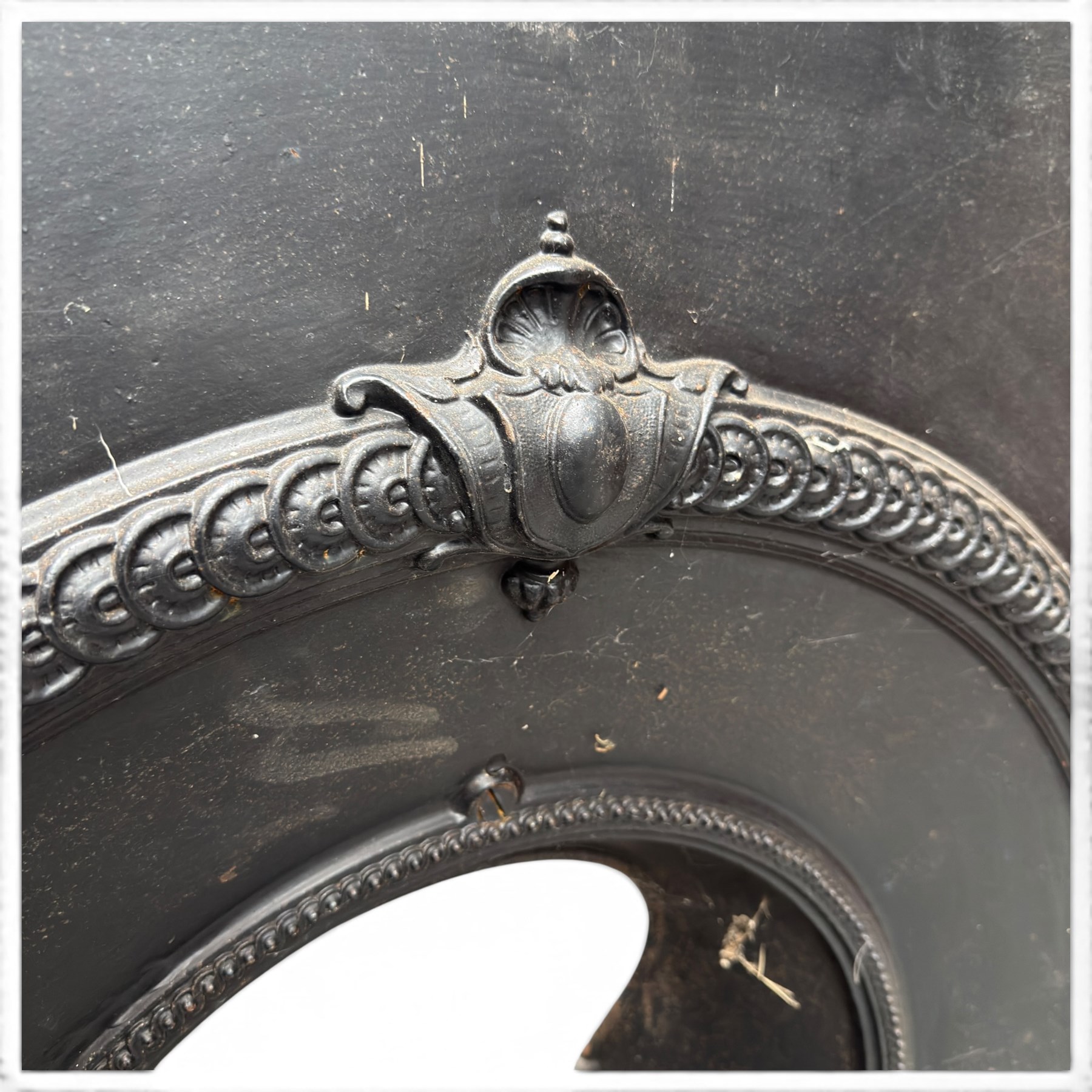 Late Victorian black-painted cast iron fireplace, the arched surround with anthemion cartouche and guilloche-moulded border, enclosing a bow-front fire basket with finialled standards, railed front and leaf-cast apron, with sheet-metal backplate