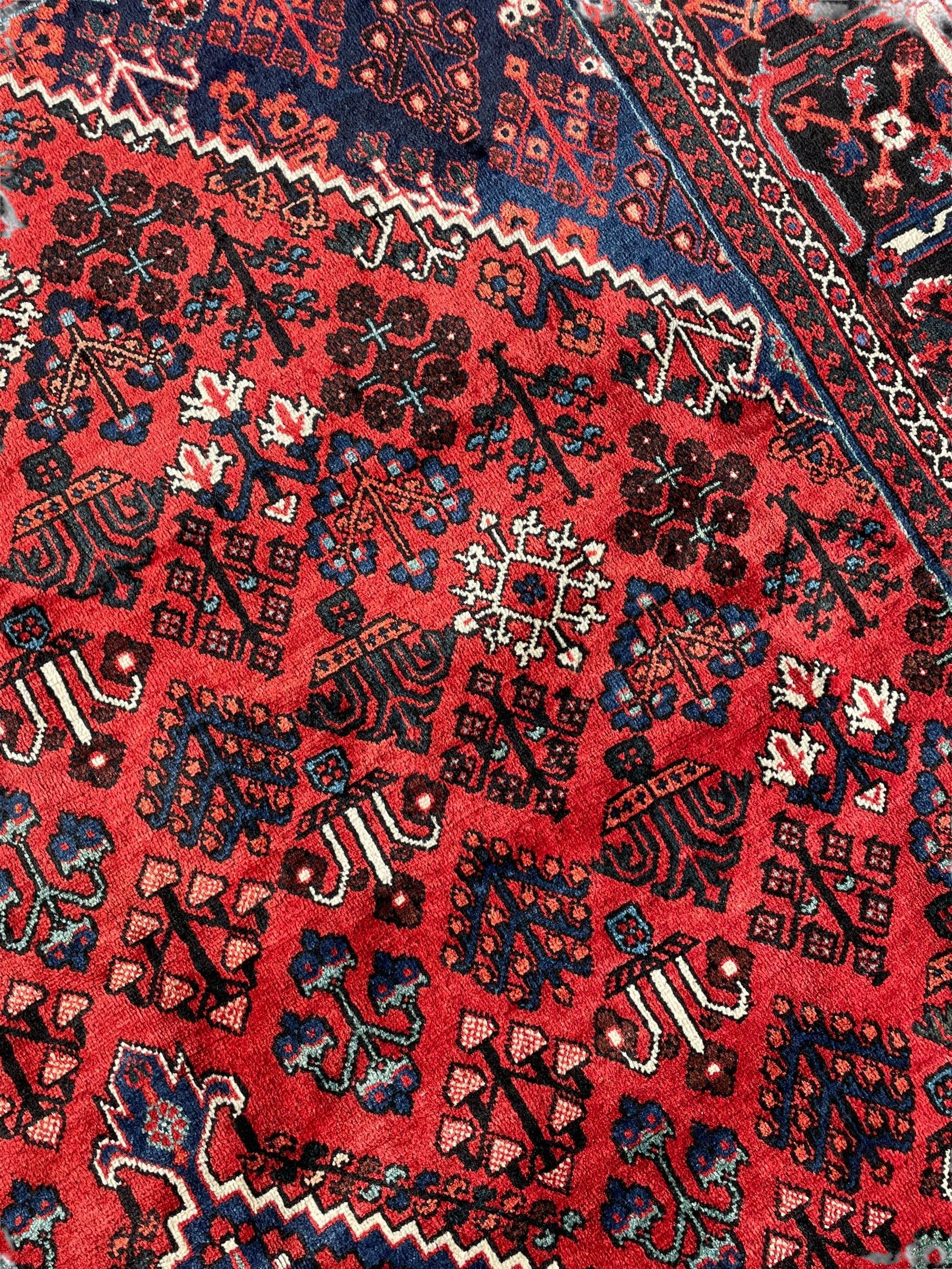 Persian Joshaghan crimson ground rug, stepped lozenge medallion surrounded by repeating foliate lozenge motifs, the border decorated with stylised plant motifs, within geometric guard stripes