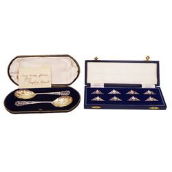 Set of eight modern silver place card holders, of pierced scrolling design, hallmarked Albert Edward Jones, Birmingham 1991, together with a pair of Edwardian silver preserve spoons, with fluted bowls and pierced scrolling handles, hallmarked Elkington & Co Ltd, Birmingham 1908, both contained within fitted silk and velvet lined fitted cases