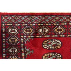 Afghan Bokhara crimson ground carpet, the field decorated with eight Gul motifs with surrounding geometric woven guard bands
