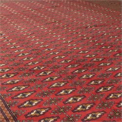 North East Persian Turkoman hand-knotted carpet, madder red field decorated with rows of repeating Tekke guls, in offset horizontal bands and interspersed cruciform subsidiary motifs, enclosed within narrow geometric borders featuring stylized tribal devices, with fringe ends   