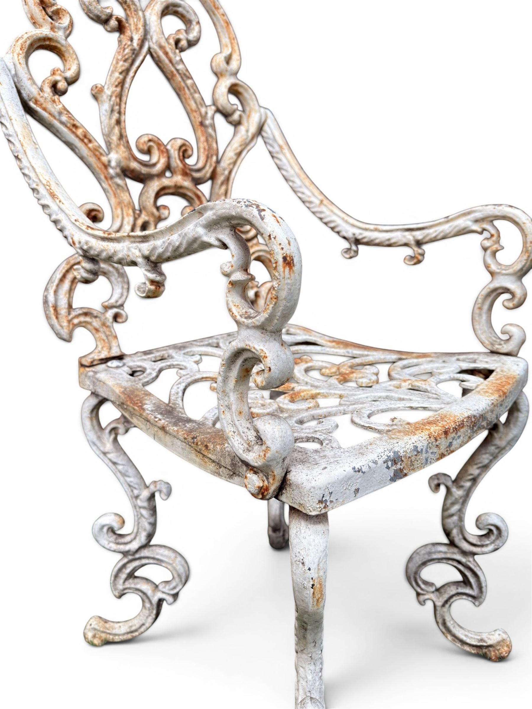 Pair of Victorian cast iron garden chairs, the ornate pierced back of scrolling foliate design, scrolling arm terminals over splayed supports formed of C and S-scrolls, in distressed white painted finish