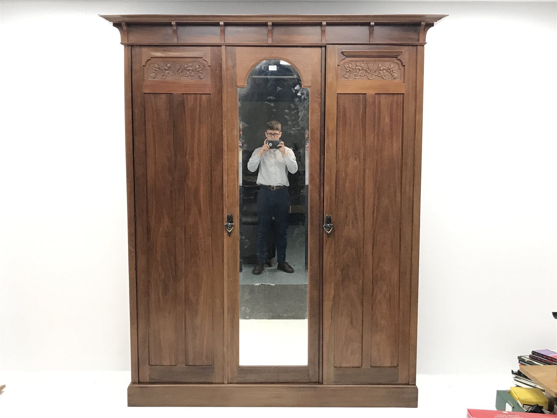 Irish Arts & Crafts walnut triple wardrobe circa 1908, projecting cornice above three doors enclosing fitted interior, single full length bevel edge mirror, platform base, W173cm, H204cm, D56cm