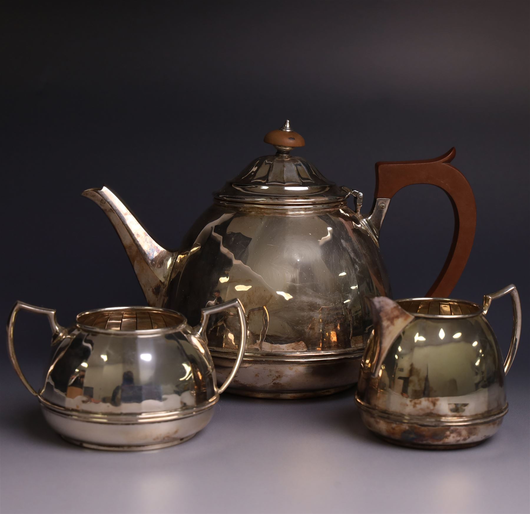 Art Deco three piece silver batchelors tea service, comprising teapot, milk jug and open sucrier, each of faceted form, the teapot with Bakelite handle and wooden finial, hallmarked Barker Brothers Silver Ltd, Birmingham 1933
