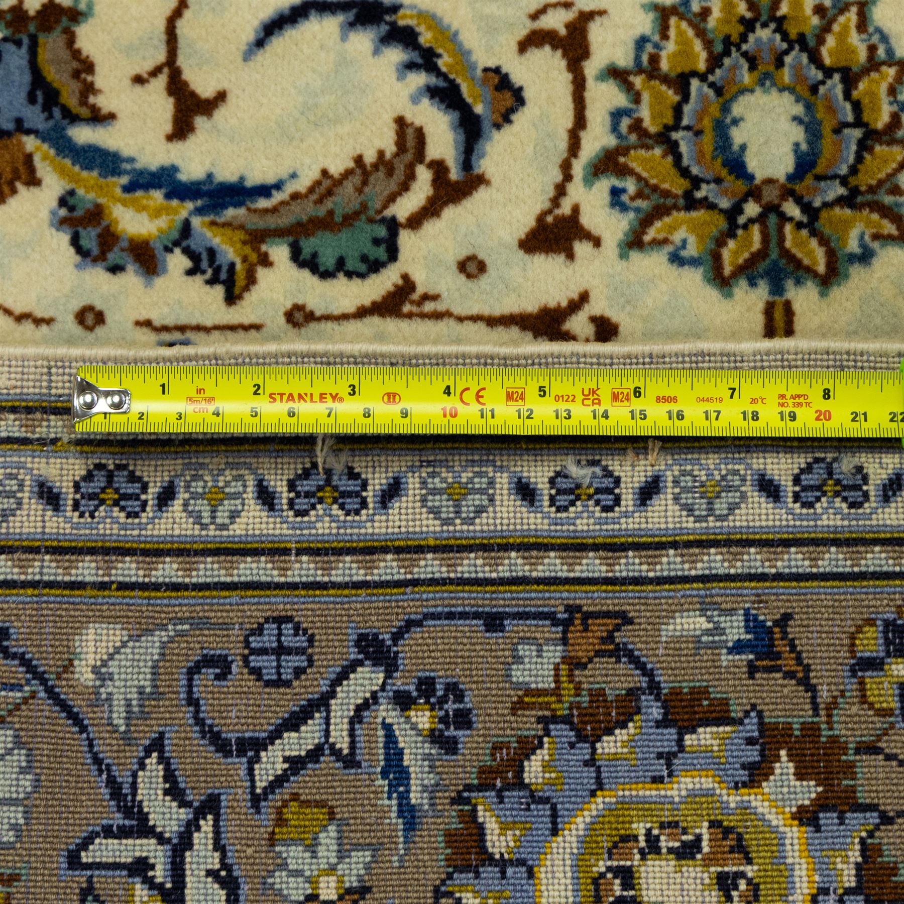 Central Persian Kashan hand-knotted carpet, ivory ground, with an all-over floral design of palmettes, scrolling vines and flowerheads in blue, ochre and beige tones, enclosed by a sage green border with repeating floral sprays and leafy scrolls, flanked by narrow guard stripes, with cotton fringes