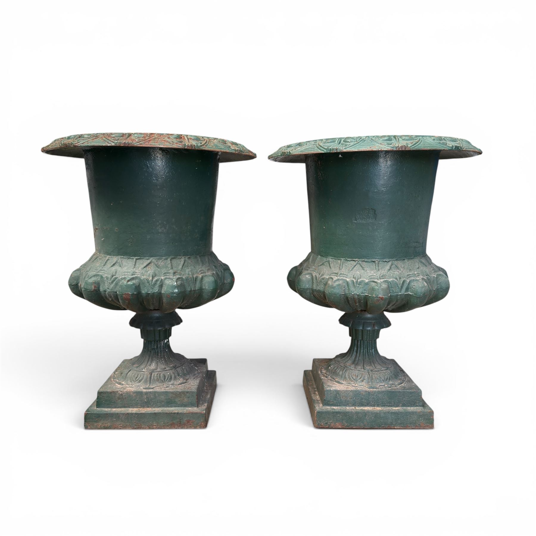 Pair of Victorian cast iron campana garden urns, the flared rim with repeating stylised anthemion motifs with scrollwork, over a deep gadrooned and Aesthetic moulded underbelly, fluted and foliate lower bowls on square pedestal bases, in antique green-painted finish