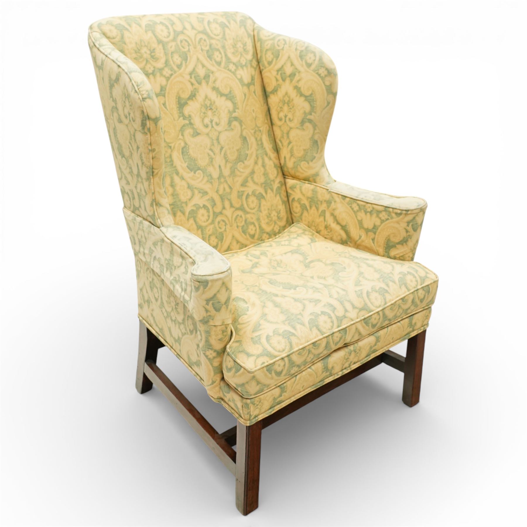 George III wing back armchair, the tall upholstered back with deep wings and gently shaped outline, padded arms flowing into the seat, loose cushion seat upholstered in a foliate patterned fabric, standing on square legs joined by stretchers