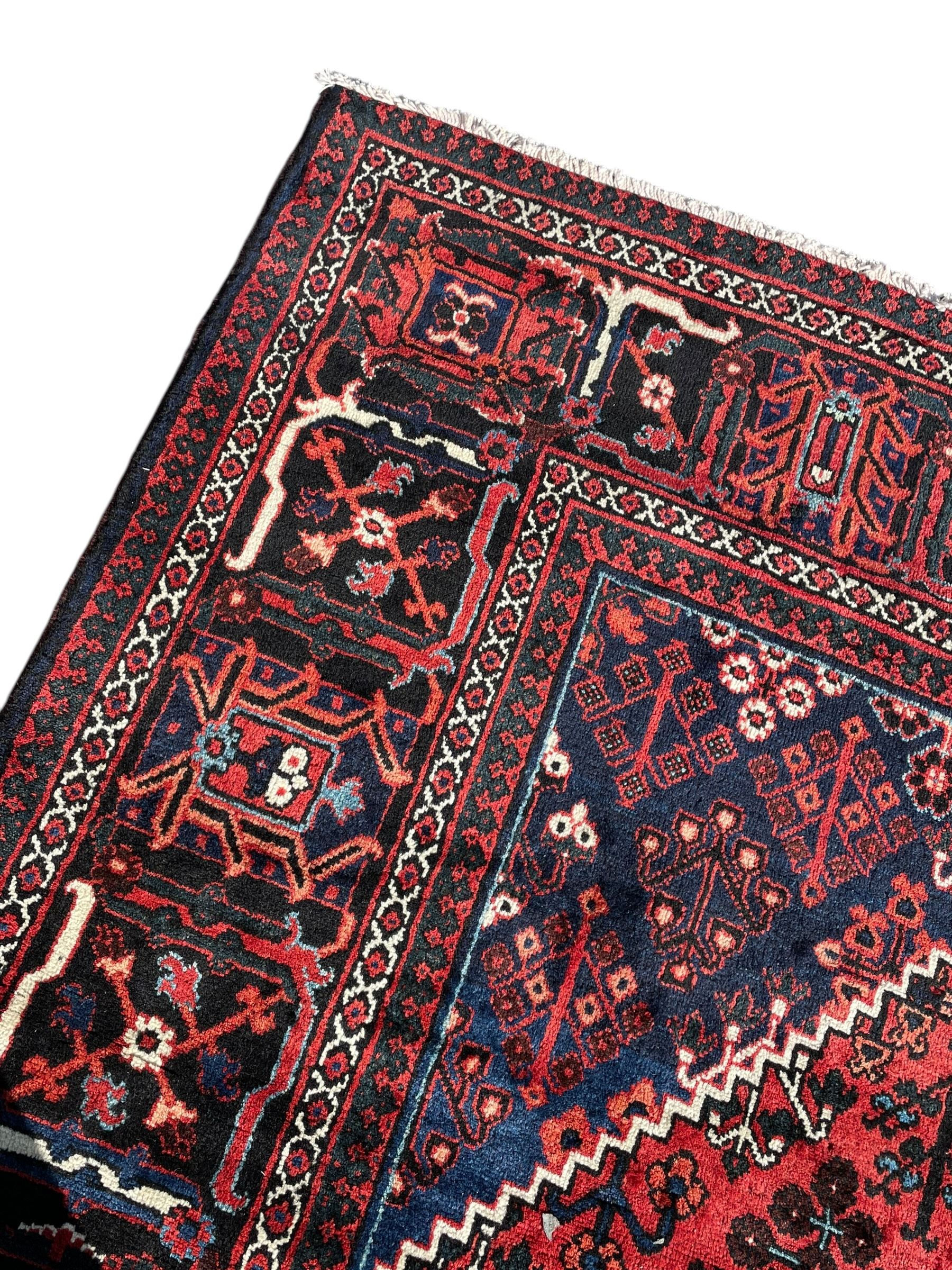 Persian Joshaghan crimson ground rug, stepped lozenge medallion surrounded by repeating foliate lozenge motifs, the border decorated with stylised plant motifs, within geometric guard stripes