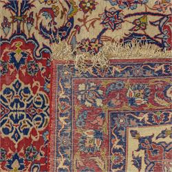 Kashan design wool rug, with red floral medallion on a cream field, decorated with scrolling foliate motifs in blue, red and green tones, enclosed by red and blue floral borders with fringed ends