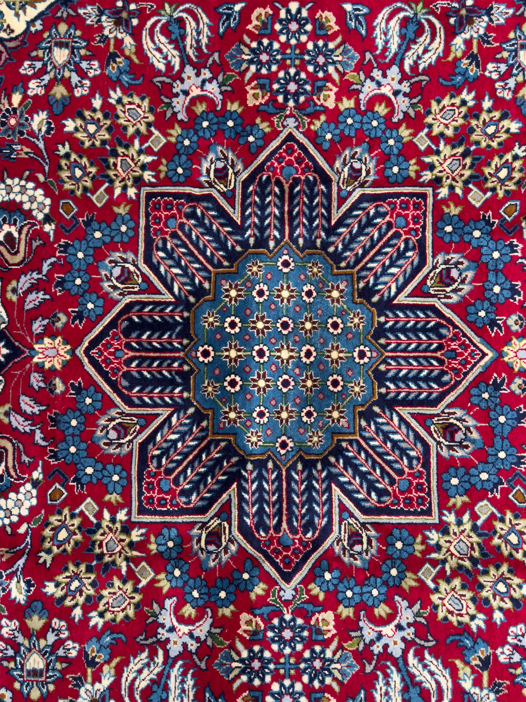 Central Persian Isfahan Carpet, hand-knotted, featuring a bold central rosette medallion on a rich red field, flanked by stylised floral sprays, scrolling foliage and mythical animals, within a broad indigo border decorated with alternating cartouches and flowerheads