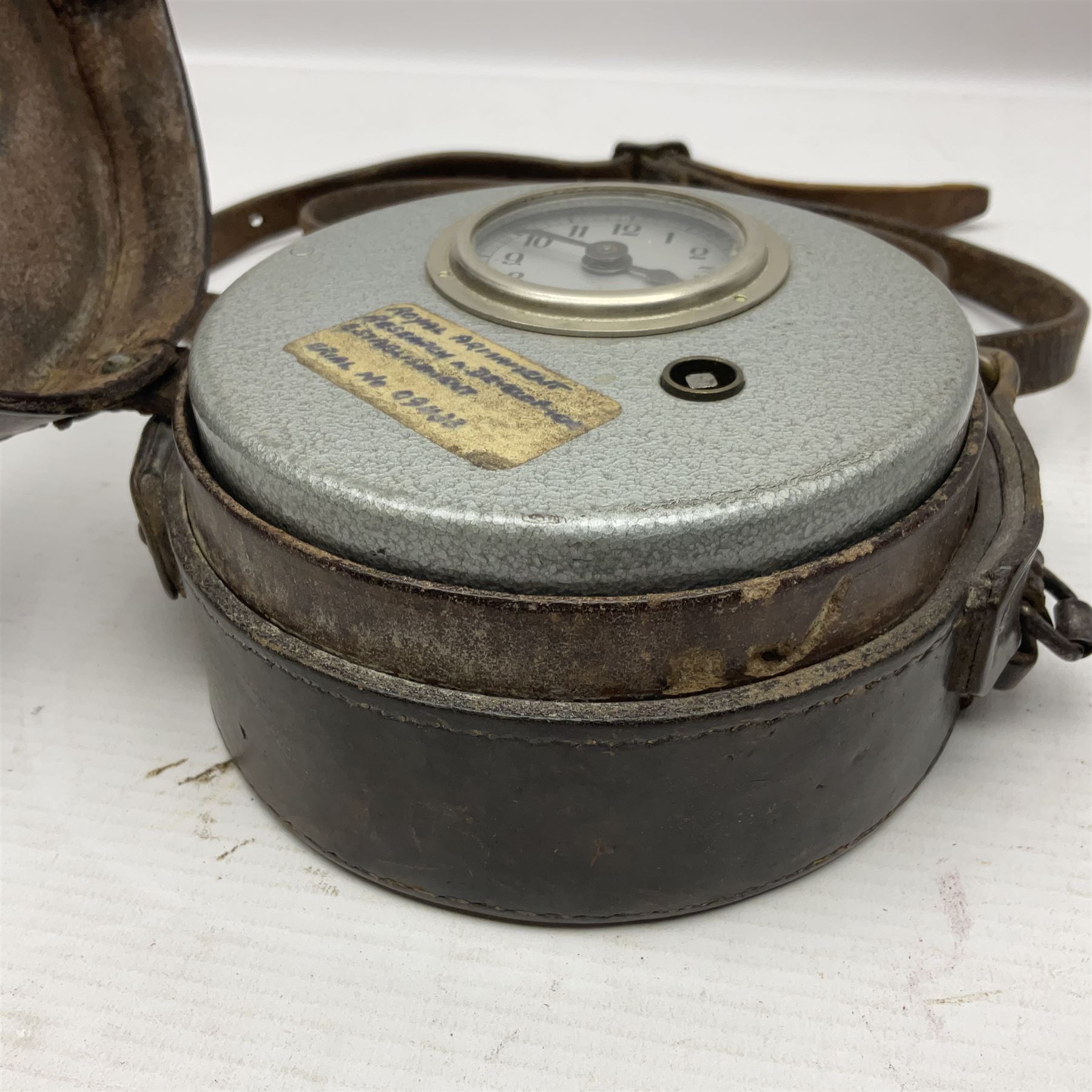 Metal cased drum shaped travelling clock with grey hammered finish, French clockwork movement and stitched leather outer case with shoulder strap; bears manuscript label 'Royal Armament Research and Development Establishment - serial no.09433' D13cm overall