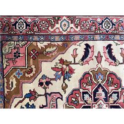 Northwestern Persian Heriz hand-knotted rug,  ivory field with a bold stepped medallion in madder red, navy and pale blue, surrounded by angular floral motifs and stylized leaves, the spandrels in camel and rose with a madder-red border of rosettes and angular vine motifs between multiple guard stripes, 180cm x 156cm