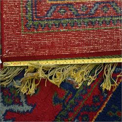 Indian Kayam rug, the rectangular field with repeating geometric medallions on a red ground, within a blue border of stylised floral motifs, with guard borders and fringe terminals