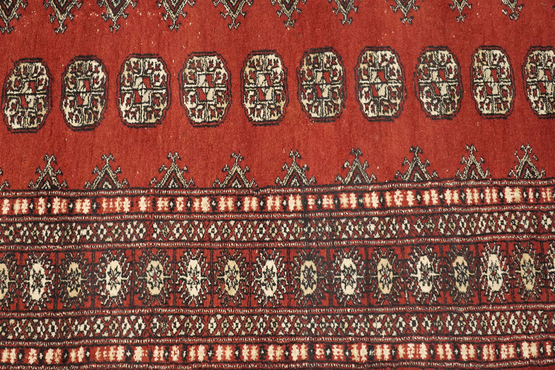 Turkoman hand-knotted rug, madder red ground with two rows of repeating octagonal guls interspersed with geometric motifs, enclosed by multiple geometric and stylised floral borders, with fringed ends