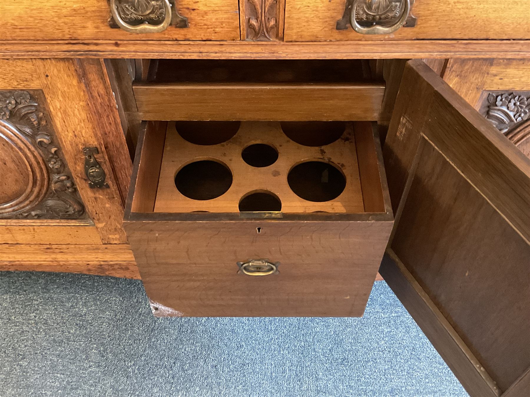 Late 19th century Arts & Crafts period oak mirror back sideboard, shaped bevelled mirror back carved with foliate scrolls and flower heads, down swept supports with elongated club-shaped uprights, moulded rectangular top over two drawers and three cupboards, the drawer fronts with copper handles decorated with sailing ships, panelled doors carved with mythical beasts, flowerheads and foliage, on moulded block feet