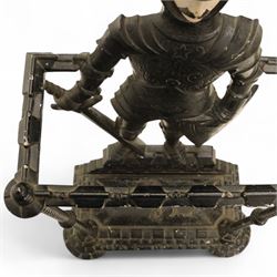Early 20th century painted cast iron hall stand, formed as a standing armoured figure with red and yellow feathered crest, twin rails and integral drip tray with castellated edge