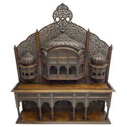 Late 19th century Indian Burmese carved and pierced hardwood and brass inlaid wall shelf, the shaped back profusely decorated with trailing and interlaced foliage, with projecting architectural structures, the central balcony with canopy top and five open windows with arched apertures on columns, two flanking five-sided balconies, the shelf supported by six foliate carved columns with pierced cusped pointed arches 
