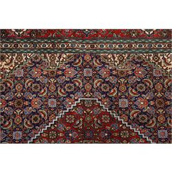 North West Persian Tabriz hand-knotted rug, ivory field with a central lozenge medallion in deep indigo and madder red, enclosing a inner reserve with stylized floral motifs, spandrels with angular floral sprays, main border of repeating floral vinery and palmettes, framed by multiple guard borders, with cotton fringe ends