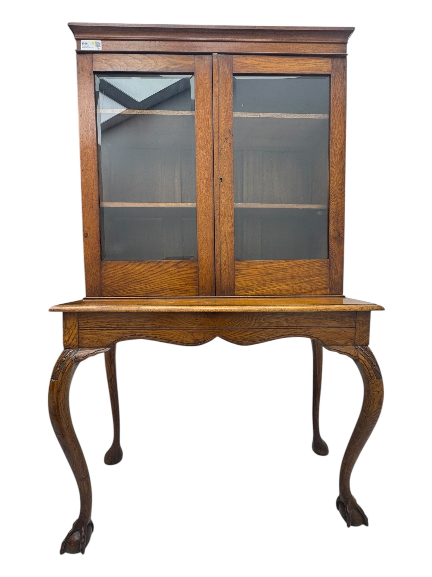 Late 19th century oak display cabinet, rectangular form with a pair of glazed doors enclosing shelves, raised on cabriole supports with carved detailing ending in claw feet