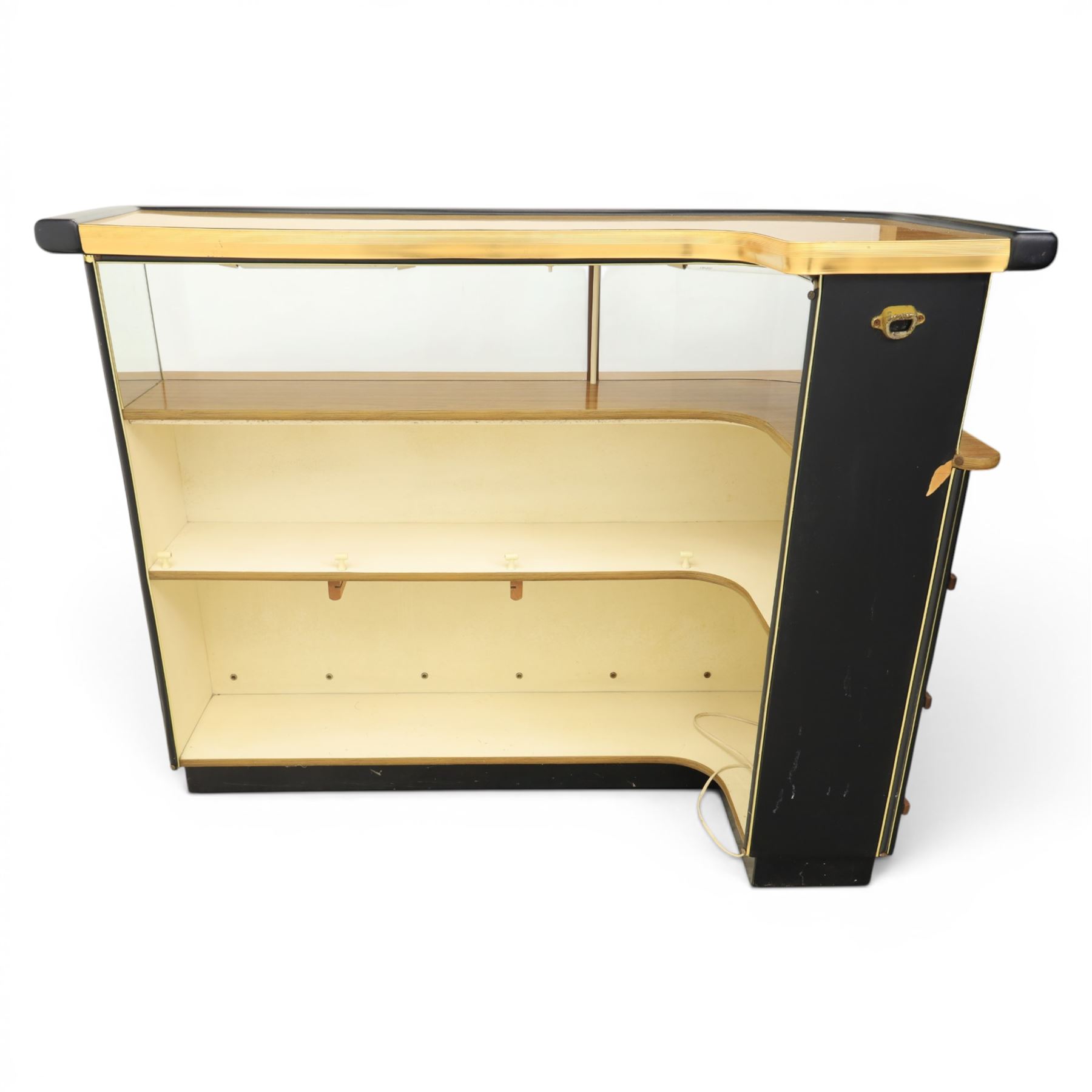 Barget of London - Mid 20th century L-shaped teak and black vinyl cocktail bar, shaped top with gilt metal banding and black cushioned edge over glazed upper section and open serving shelf, the reverse fitted with shelves, the front with applied lattice mouldings over black vinyl, on plinth base