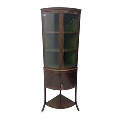 Edwardian mahogany bow front standing corner cabinet, projecting cornice with Greek key moulding decoration, two glazed doors with ebony and satinwood stringing enclosing two shelves, over cupboard and under-tier 