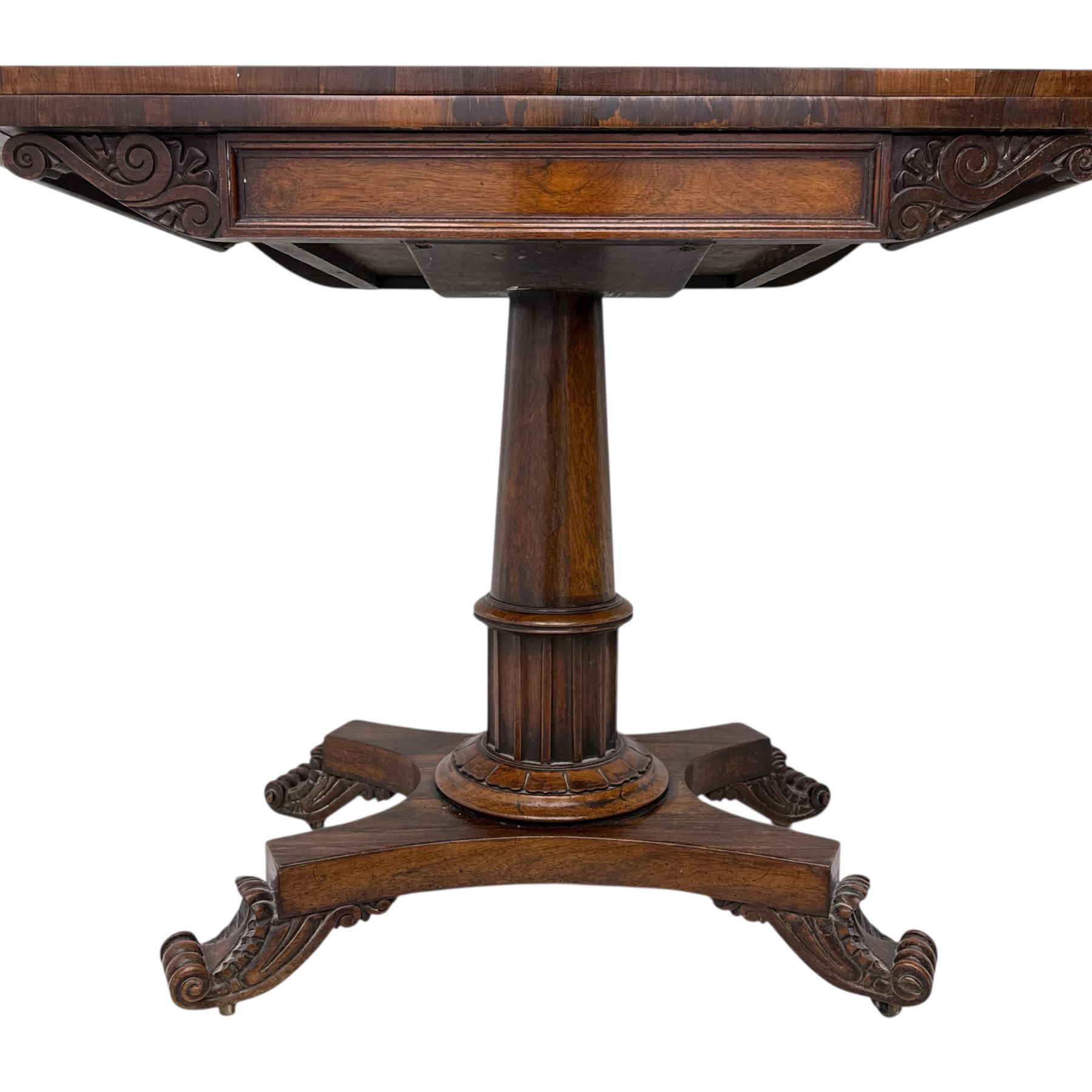 William IV rosewood card table, rounded rectangular swivel and fold-over top with plain frieze, with carved scrolled brackets above stop-fluted column with moulded collar on quadriform base with scrolled feet 