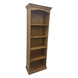 Early 20th century pine bookcase, projecting cornice over arched open shelving area with four fixed shelves, on shaped plinth base