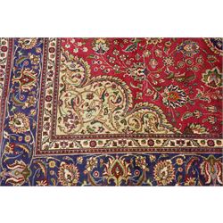 North East Persian Meshad hand-knotted carpet, crimson field with central lobed medallion in tones of indigo, ivory and soft blue, with an all-over arrangement of scrolling vinery, palmettes, and floral  sprays, conforming spandrels, main border of stylized floral vinery framed by multiple guard borders, with cotton fringe ends