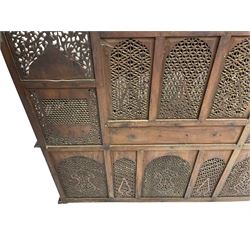 Late 19th century Indian Burmese carved and pierced hardwood and brass inlaid wall shelf, the shaped back profusely decorated with trailing and interlaced foliage, with projecting architectural structures, the central balcony with canopy top and five open windows with arched apertures on columns, two flanking five-sided balconies, the shelf supported by six foliate carved columns with pierced cusped pointed arches 