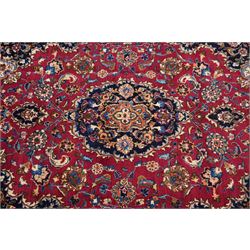 Central Persian Kashan hand-knotted carpet, rose red field, with central shaped lobed medallion issuing an all-over scrolling design of palmettes, floral sprays and arabesques, within conforming spandrels, enclosed by a broad indigo herati type palmette border framed by multiple guard stripes, in a palette of deep red, midnight blue and ivory tones, with cotton fringe ends, and Kashan signature 