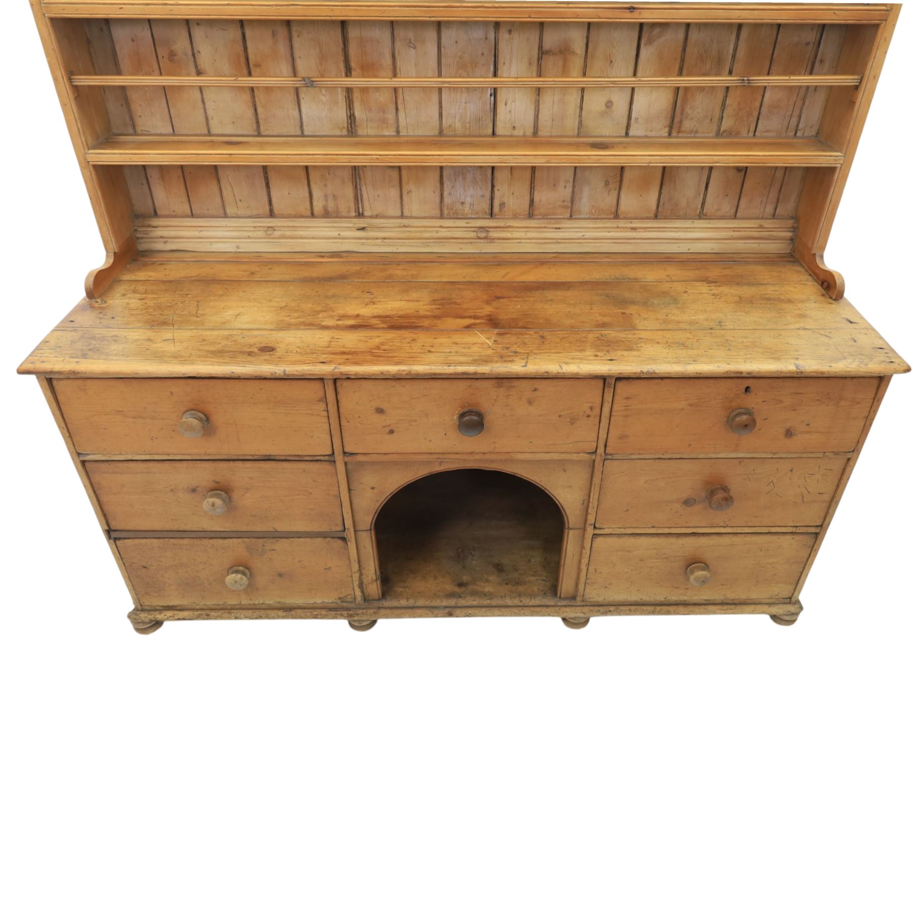 Early 19th century waxed pine farmhouse dresser and rack, the rack featuring two plate shelves and bars above seven drawer base with centre 'dog kennel' recess, raised on turned feet