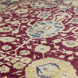 Agra design wool carpet, burgundy field decorated with large scrolling floral vines, palmettes and flowerheads, enclosed by blue main border with oversized stylised palmettes and narrow guard stripes