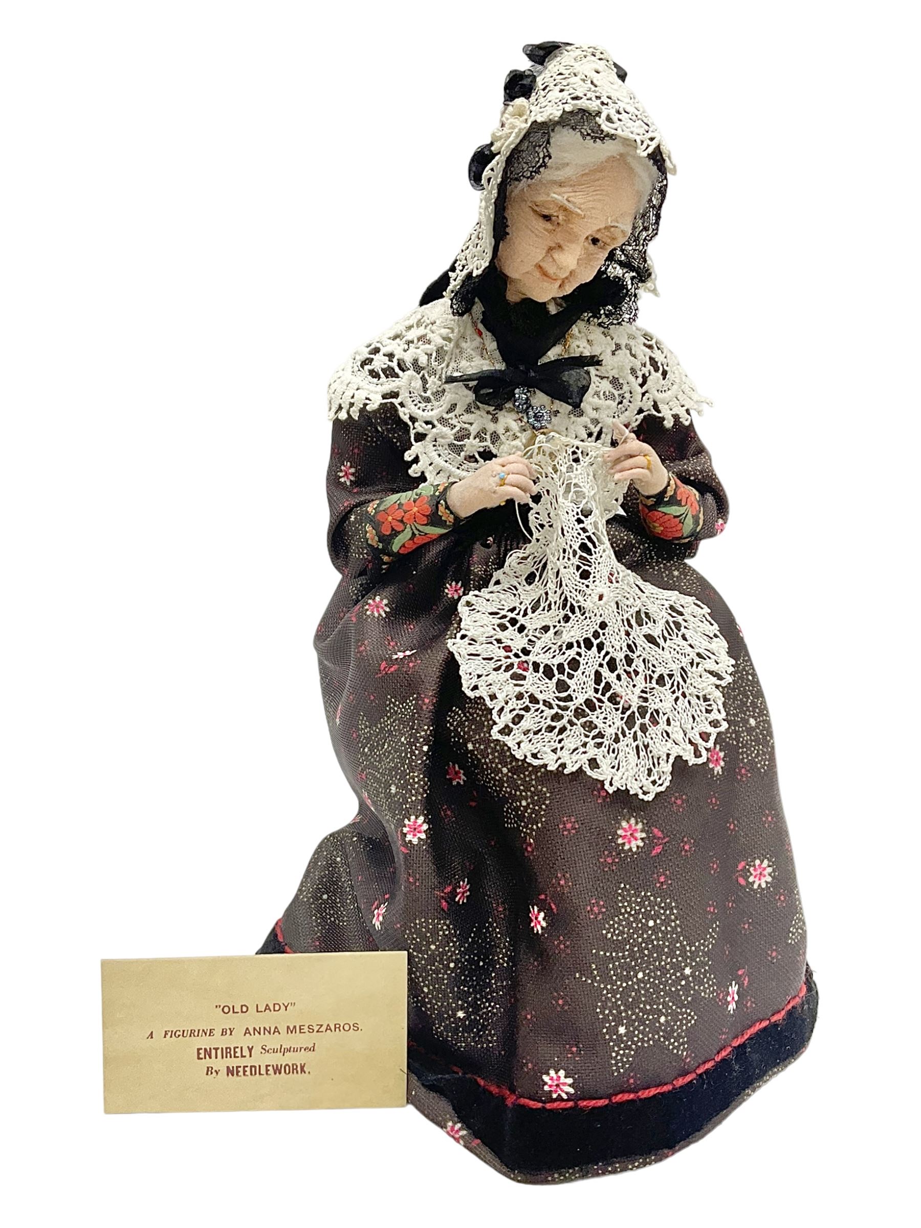 Anna Meszaros Hungary - hand made needlework figurine 'Old Lady' seated on a stool wearing a lace trimmed black/white/red floral full length dress and hat, working on a piece of lace H30cm  Auctioneer's Note: Anna Meszaros came to England from her native Hungary in 1959 to marry an English businessman she met while demonstrating her art at the 1958 Brussels Exhibition. Shortly before she left for England she was awarded the title of Folk Artist Master by the Hungarian Government. Anna was a gifted painter of mainly portraits and sculptress before starting to make her figurines which are completely hand made and unique, each with a character and expression of its own. The hands, feet and face are sculptured by layering the material and pulling the features into place with needle and thread. She died in Hull in 1998.