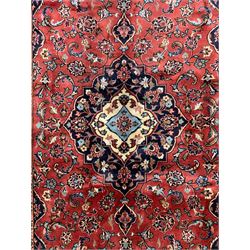 Persian Ardakan crimson ground rug, the field with shaped floral design medallion surrounded by curled leafy branches, scrolling border with stylised plant motifs