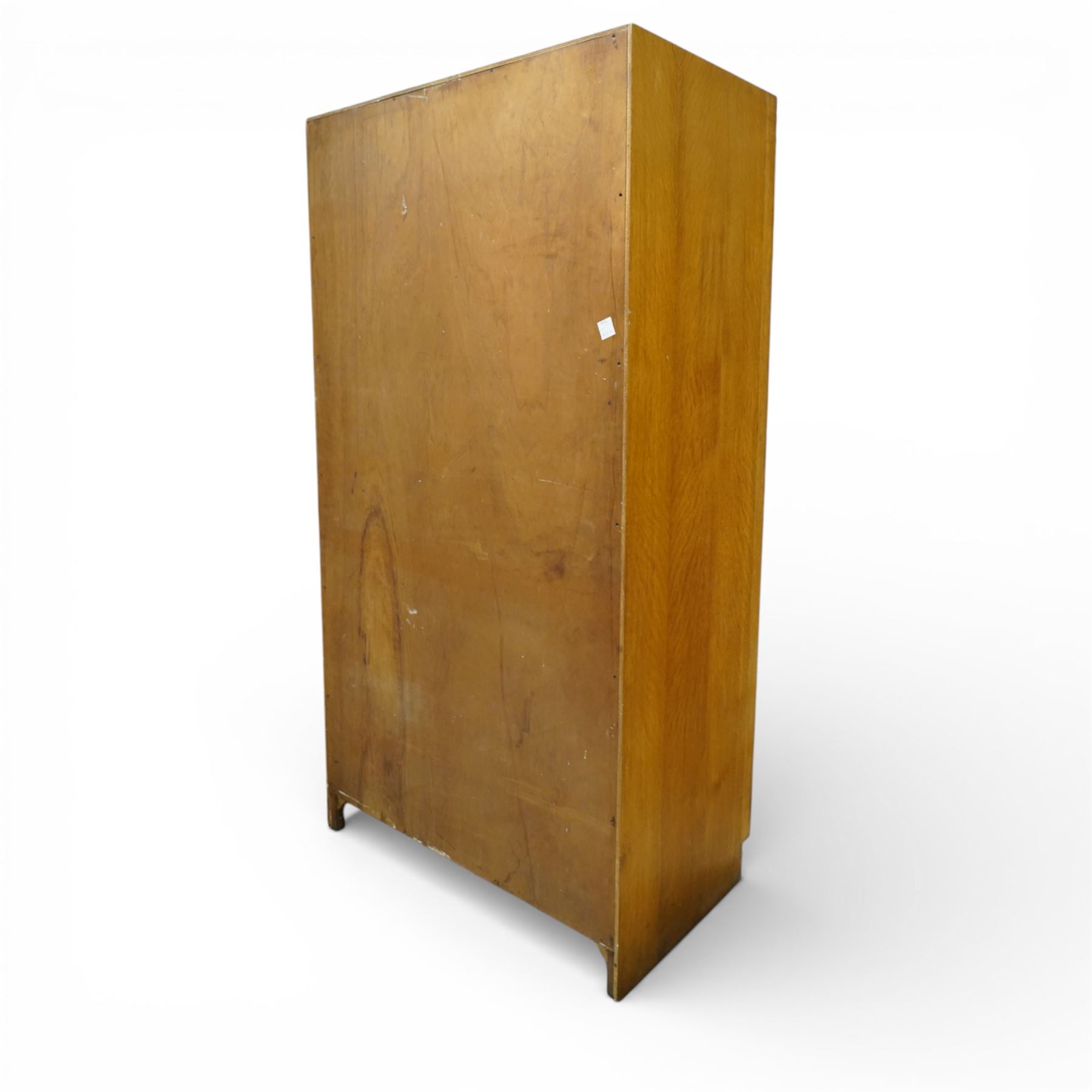Mid 20th century oak veneered wardrobe, the plain rectangular top above a pair of hinged doors fitted with circular handles, opening to reveal a hanging rail and upper shelf, one door with inset mirror, the whole raised on a plinth base