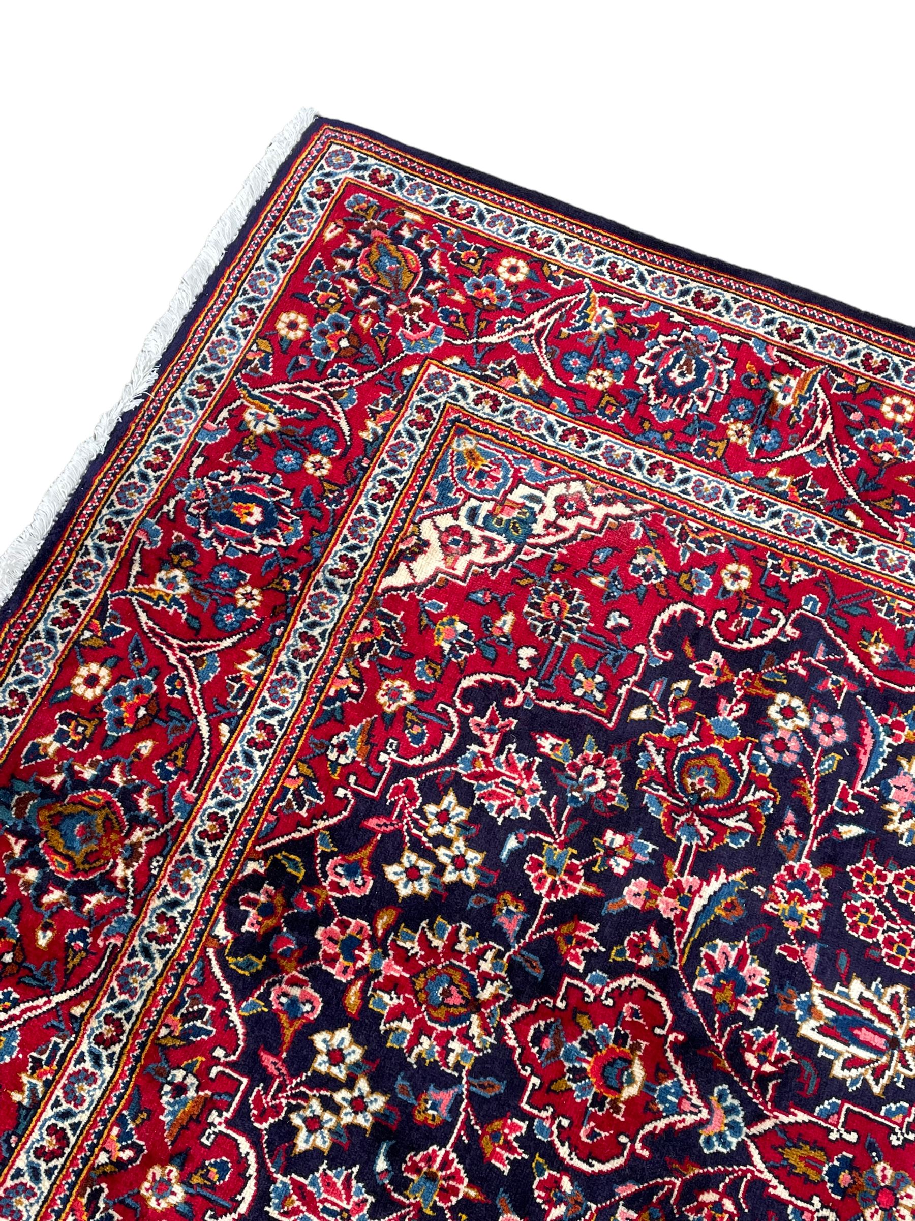 Persian indigo ground rug, the central crimson pole lozenge medallion surrounded by interlacing floral patterns, the main border with repeating plant motifs connected by scrolling branches
