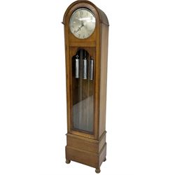 German - 1930s 8-day chiming longcase clock in an oak case, with a break arch top and fully glazed door, plinth raised on bun feet, circular silvered dial with Arabic numerals and pierced steel hands, three train weight/chain driven movement sounding the quarters and hours on 12 gong rods, with chrome cased weights and conforming pendulum. 