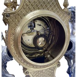 A 20th century continental gilt metal Lyre mantle clock with a pair of matching six light candelabra, spring driven movement housed in a gilt drum case on a brass and cobalt blue base with paw feet, two bronzed metal figures of mythological cherubs with animal legs and cloven hooves supporting a festooned garland swag, eight-day twin barrel striking movement with a floating lever balance escapement, striking the hours and half-hours on two bells, white enamel dial with roman numerals, minute track and pierced steel hands, dial inscribed “Imperial”. 