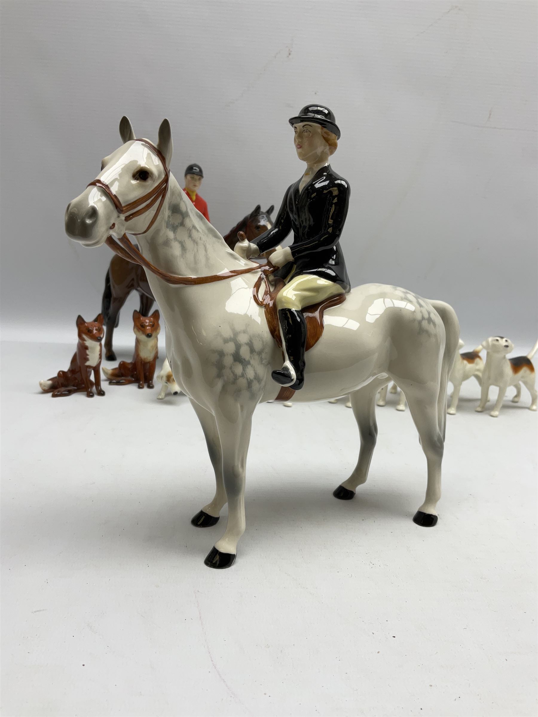 Beswick hunting group, comprising huntswoman on grey horse no 1730, huntsman on brown horse no 1501, two seated fox figures no 1748 and seven fox hounds, all with printed marks beneath (11)