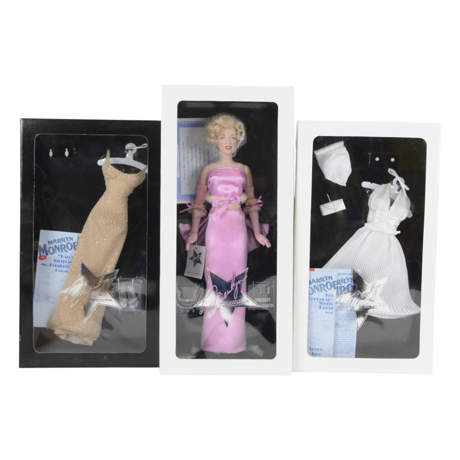 Franklin Mint Marilyn Monroe portrait doll, dressed in Gentleman Prefer Blondes pink dress, together with a wardrobe trunk and four outfits, comprising white dress from The Seven Year Itch, black dress from Some Like It Hot, red glitter dress with feather headress from The Seven Year Itch and the 'Happy Birthday Mr President' nude dress, all boxed with certificate of authenticity